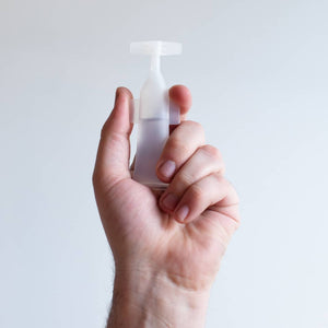 Hand holding a single translucent Activator Capsules 25ct box 12oz/3mL | Force of Nature capsule against a plain light background, showcasing the product's sleek design.