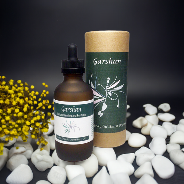 Garshan Body Oil | Red Cherry Group in a brown dropper bottle with green label beside matching cylindrical packaging, surrounded by white stones and yellow flowers on a dark background