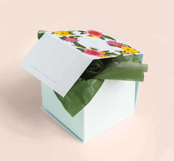 White gift box with floral design on the lid and green tissue paper inside, showcasing the Honey I’m Smooth Limited Edition Set | Farmhouse Fresh for skincare and body care.