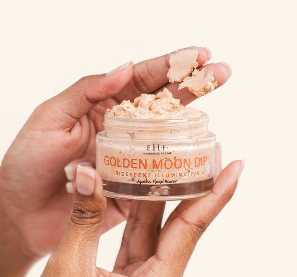 Close-up of hands holding an open jar of Golden Moon Dip® Illumination Mousse with Retinol + Wrinkle-Targeting Peptides | Farmhouse Fresh, showing creamy, iridescent skincare mousse texture.