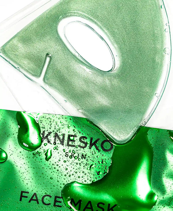 Close-up of a shimmering green gel face mask sheet with an eye cutout resting on its glossy green packaging labeled Green Jade Calm Face Mask | KNESKO, showcasing skincare and wellness.