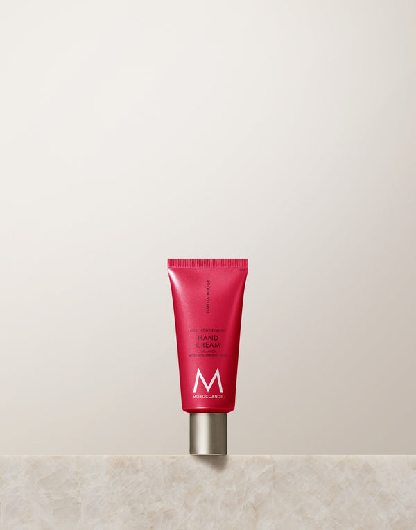 Red tube of Hand Cream | Moroccanoil standing upright on a marble surface against a neutral background, emphasizing skincare and body care products.