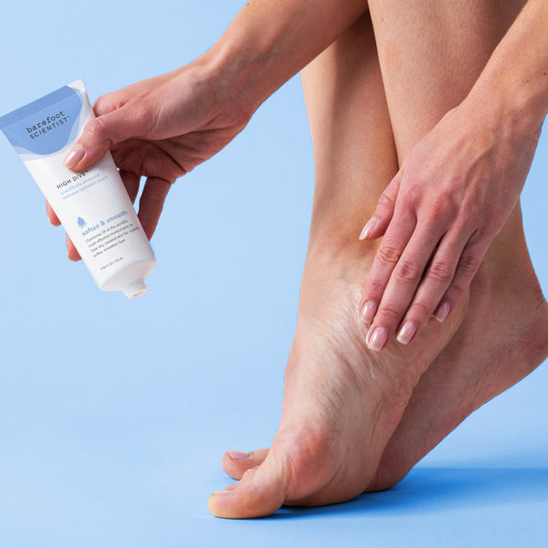 Person applying High Dive Intensive Hydration Cream | Barefoot Scientist to dry skin on foot against a light blue background for skincare and body care wellness.