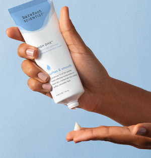 Hand holding and dispensing a small amount of High Dive Intensive Hydration Cream | Barefoot Scientist onto the fingertip against a soft blue background.