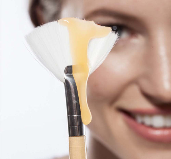 Honey I’m Smooth Limited Edition Set | Farmhouse Fresh creamy golden skincare mask applied on a soft fan brush held near a smiling woman's face for body care and wellness.