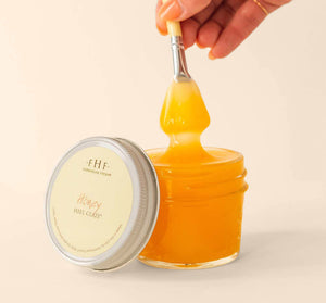 Close-up of a hand holding a spatula dipping into a jar of golden honey-like skincare product labeled Honey I’m Smooth Limited Edition Set | Farmhouse Fresh, designed for nourishing body care.