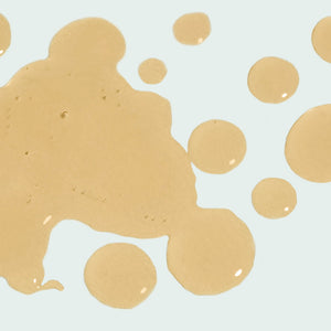 Close-up of golden liquid drops on a light background, representing the texture of ILUMA intense facial illuminator | IMAGE Skincare skincare product.