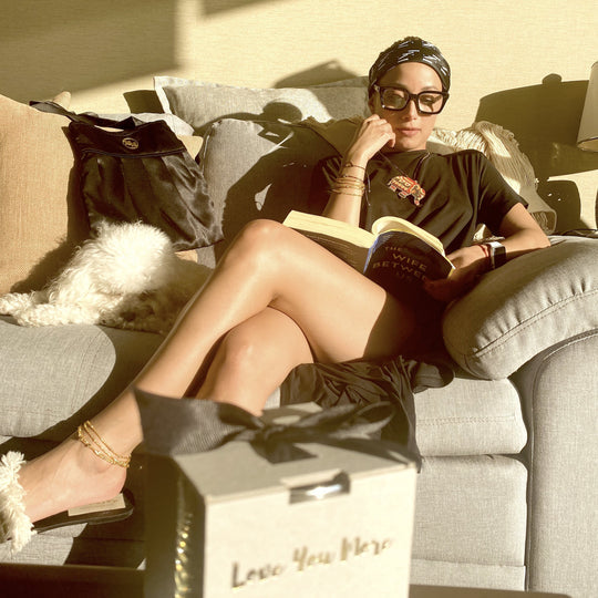 Woman wearing Chic Trendy Reading Glasses | Love You More while reading a book on a couch next to a small white dog in soft natural light