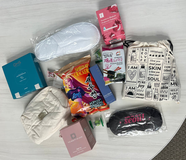 2026 Destination Wellness Box including skincare products, wellness supplements, a white quilted pouch, slippers, a sleep mask with Seoul text, and a drawstring bag with wellness affirmations.
