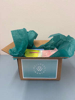 Open cardboard box with teal tissue paper containing wellness products and labeled for 2026 Wellness Month Box ($1,100+ Value) | Live Love Spa.