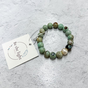 Bracelet featuring round, earthy green and brown beads with a single pearl accent, accompanied by a tag, showcasing the Opal Luxe Bracelet | Be the Light.