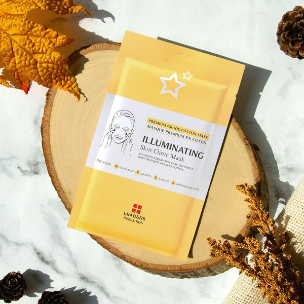 Illuminating Skin Clinic Mask | Leaders packaged in a yellow and white pouch placed on a wooden round board with autumn leaves and natural decor accents in soft natural light.