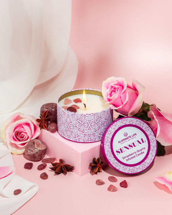 Sensual Candle Tin 6 oz | Aluminate Life featuring a lit candle with strawberry quartz stones, surrounded by pink roses and star anise for a soothing and romantic ambiance.