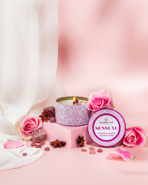 Sensual Candle Tin 6 oz | Aluminate Life with a lit strawberry quartz infused candle surrounded by pink roses, rose petals, and aromatic spices on a soft pink background.