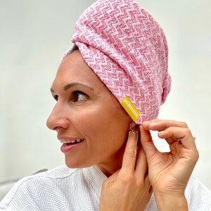 Woman wearing a pink patterned Microfiber Hair Turban | Popmask, adjusting it near her ear, promoting a comfortable and stylish hair care accessory for skincare and wellness routines.