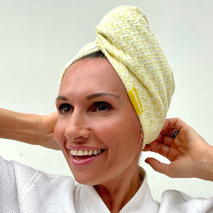 Smiling woman adjusting a soft yellow microfiber hair turban | Popmask on her head, showcasing a comfortable and stylish hair care accessory for skincare and wellness routines.