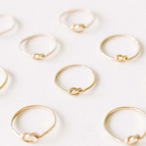 Multiple delicate gold rings arranged on a light surface, each featuring a simple knot design, showcasing the Knot Ring | Purpose Jewelry.