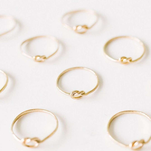 Multiple delicate gold rings arranged on a light surface, each featuring a simple knot design, showcasing the Knot Ring | Purpose Jewelry.