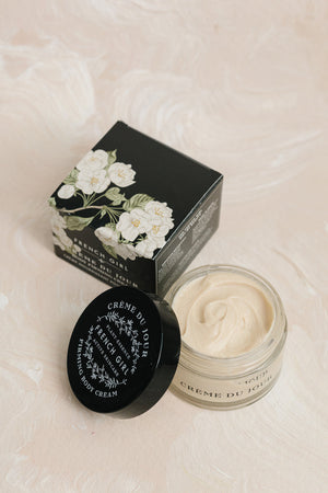 Open jar of Body Firming Cream | French Girl with a black floral box beside it on a soft beige surface, showcasing the smooth cream texture and elegant packaging for skincare.