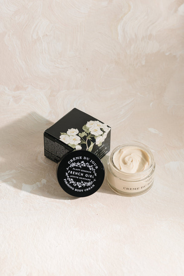Open jar and closed container of Body Firming Cream | French Girl with floral design on black box and cream texture visible against a light textured background.