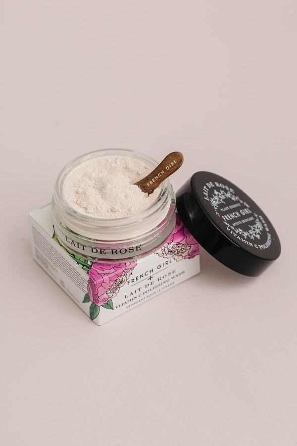 Open jar of Vitamin C Polishing Facial Wash & Mask | French Girl with light powder inside and a small wooden spatula, placed on floral printed packaging box for skincare product.