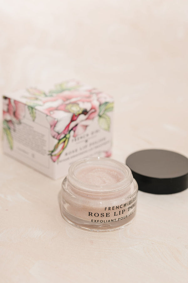 Open jar of Rose LIp Polish | French Girl lip exfoliant next to floral decorative box on light beige surface for skincare and body care wellness routine.