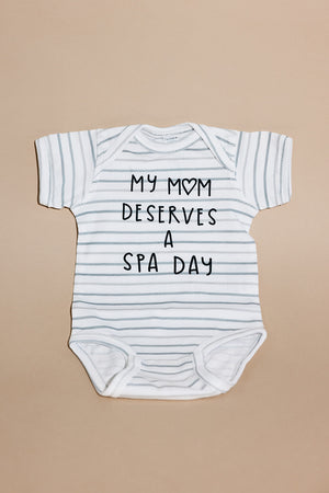 White and light gray striped baby onesie with the text "My mom deserves a spa day" printed on the front, Mom Deserves A Spa Day Baby Onesie | Lucky Owl.
