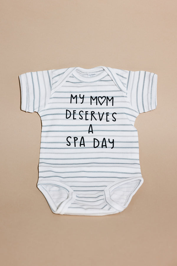 White and light gray striped baby onesie with the text "My mom deserves a spa day" printed on the front, Mom Deserves A Spa Day Baby Onesie | Lucky Owl.