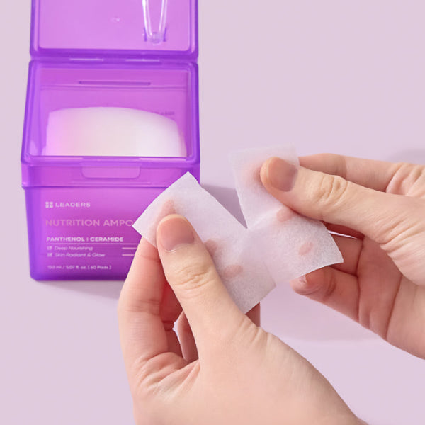 Hands holding a thin, translucent skincare pad being pulled apart next to a purple container of Nutrition Ampoule Pad | Leaders, highlighting skincare and hydration benefits.