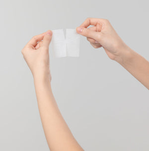Close-up of two hands gently holding and separating a white skincare pad against a plain light background, showcasing the texture of the Nutrition Ampoule Pad | Leaders.