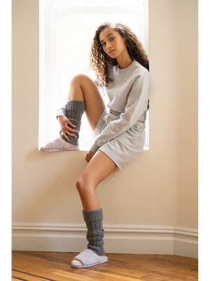 Woman wearing gray knit leg warmers and light purple Anywhere Berber Slide | Lemon slippers seated by a window in cozy casual loungewear.