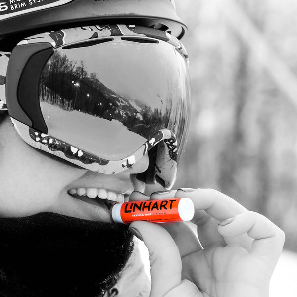 Person wearing ski goggles and winter gear applying Lip Balm SPF 15 | LINHART outdoors, highlighting skincare protection in cold weather conditions.