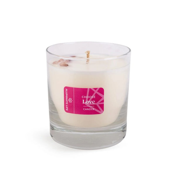 Clear glass candle with a white wax and pink label reading "Choose Love" containing small crystal accents, representing the I Choose Bliss Candle | Aluminate Life for wellness and relaxation.