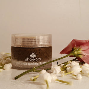 Microcrystal Exfoliator | Shankara jar surrounded by delicate white flower buds and a single pink flower, highlighting natural skincare and body care wellness.