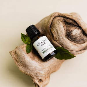 Small amber glass bottle of Essential Oil Blends | Essence One placed on natural wood with green leaves, evoking a calming and wellness-focused skincare atmosphere.