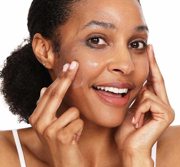 A smiling woman applying Make it Melt Silky Milk Cleansing Balm | Farmhouse Fresh to her cheek, demonstrating gentle skincare for a radiant complexion.