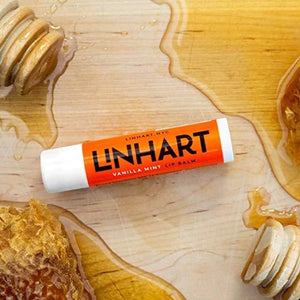 Lip Balm SPF 15 | LINHART in vanilla mint flavor placed on a wooden surface surrounded by honeycomb and honey drizzlers highlighting natural skincare and body care ingredients.