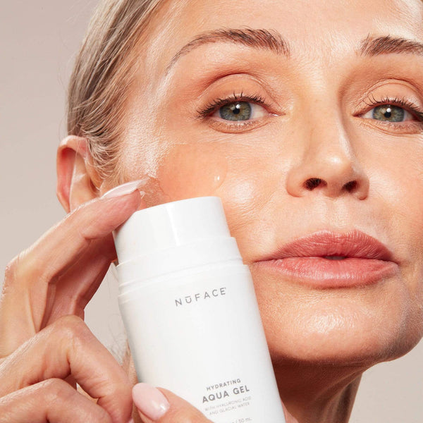 Close-up of a woman with glowing skin applying Hydrating Aqua Gel | NuFACE to her cheek, highlighting skincare and hydration benefits.
