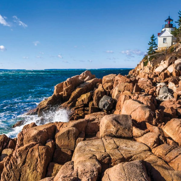 Scenic coastal view with rugged rocky cliffs and a lighthouse overlooking the ocean under a clear blue sky, evoking the serene inspiration behind Acadia 8oz Candle | The Beauty of Hope.