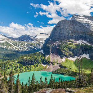 A vibrant turquoise lake surrounded by lush evergreen trees and towering snow-capped mountains under a bright blue sky, evoking the serene beauty reflected in Glacier 8oz Candle | The Beauty of Hope.