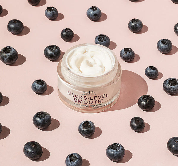Open jar of Necks-Level Smooth™ Cream | Farmhouse Fresh surrounded by fresh blueberries on a light pink background, showcasing skincare product texture and natural ingredients.