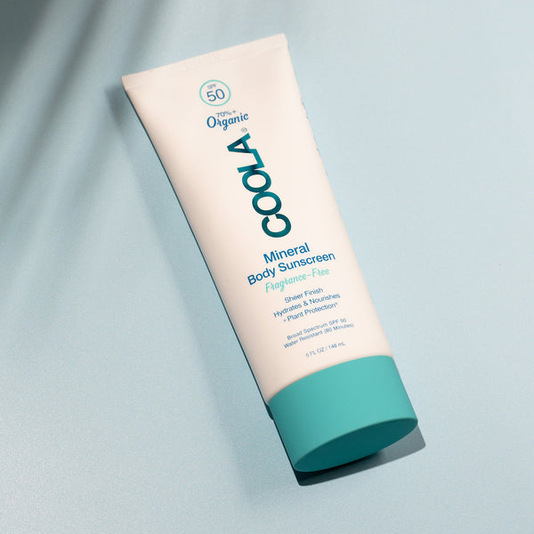 Bottle of Mineral Body Organic Sunscreen Lotion SPF 50 - Fragrance Free | COOLA lying on a light blue surface with soft natural shadows, highlighting skincare and body care wellness.