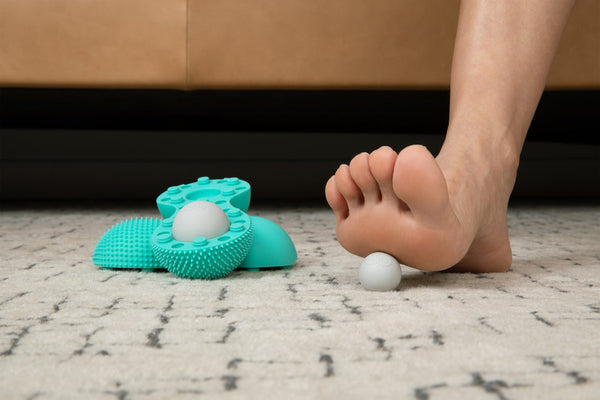 Foot rolling massage on carpeted floor using Neuro Roller | RAD wellness device with textured surfaces and white massage ball for recovery and body care.