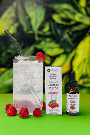 Antioxidant Green Tea Extract Water Infusion Drops - Raspberry | Pure Inventions bottle and box next to a glass of iced water with raspberries and a clear straw on a green surface with leafy background.