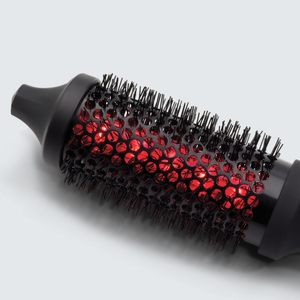 Close-up of a black round hairbrush with glowing red infrared light inside the bristles, showcasing the IR INFRARED Thermal Styling Brush 43MM | SUTRA for styling and heat therapy.