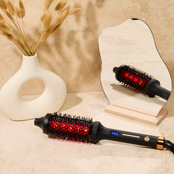IR INFRARED Thermal Styling Brush 43MM | SUTRA with black handle and red heated bristles, displayed on a beige surface next to a stylized mirror and decorative vase.
