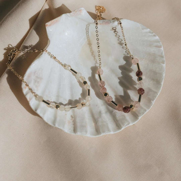 Two delicate gold chain bracelets with semi-precious stones arranged on a white seashell, showcasing Shine Bracelet | Purpose Jewelry in a soft natural light setting.