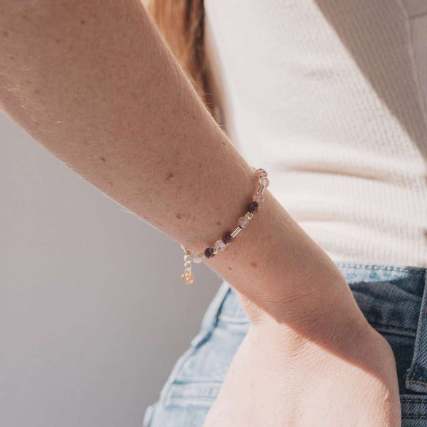 Close-up of a wrist wearing the Shine Bracelet | Purpose Jewelry with delicate beads and a small charm, paired with casual denim and a cream-colored top, highlighting mindful style.
