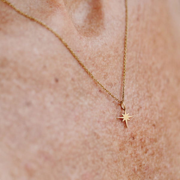 Close-up of a delicate gold North Star Necklace | Purpose Jewelry pendant on a fine chain resting on skin, symbolizing guidance and inspiration.