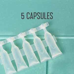 Clear plastic capsules arranged in a row on a teal tiled surface, with the text "5 CAPSULES" above, part of the 12oz Glass Bottle Cleaning Starter Kit | Force of Nature.